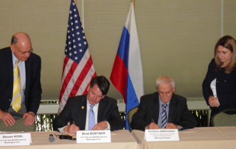 Two men seated at table signing documents.