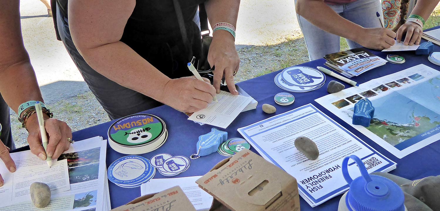 Salmonfest attendees sign postcards showing their opposition to the Susitna Dam
